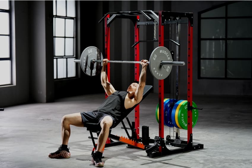 A man is siting on the weight bench to lifting a barbell on the power rack.