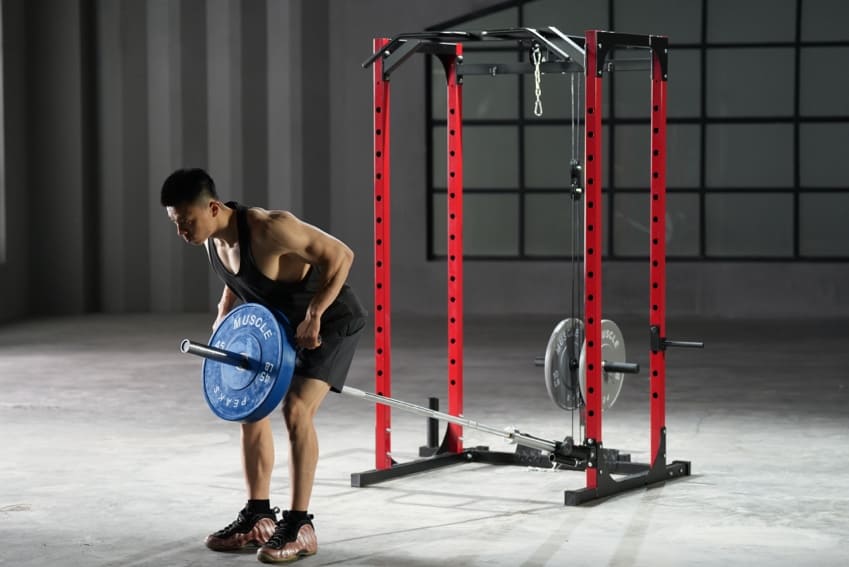 A man is using barbell bar to doing some exercise before the red and black power rack.