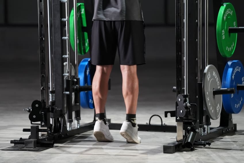 A man is showing off his leg muscles before smith machine