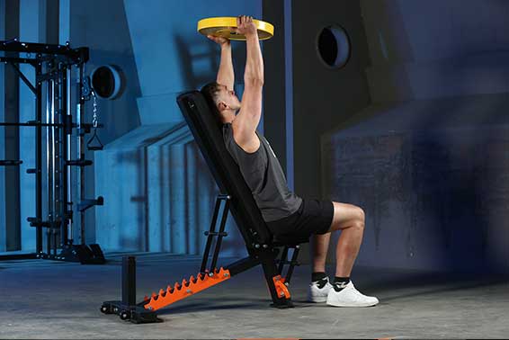 A man is lifting a barbell plate on a black adjustable bench