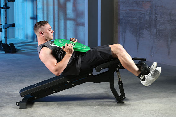 A man  is doing weighted decline sit-up on the weight bench