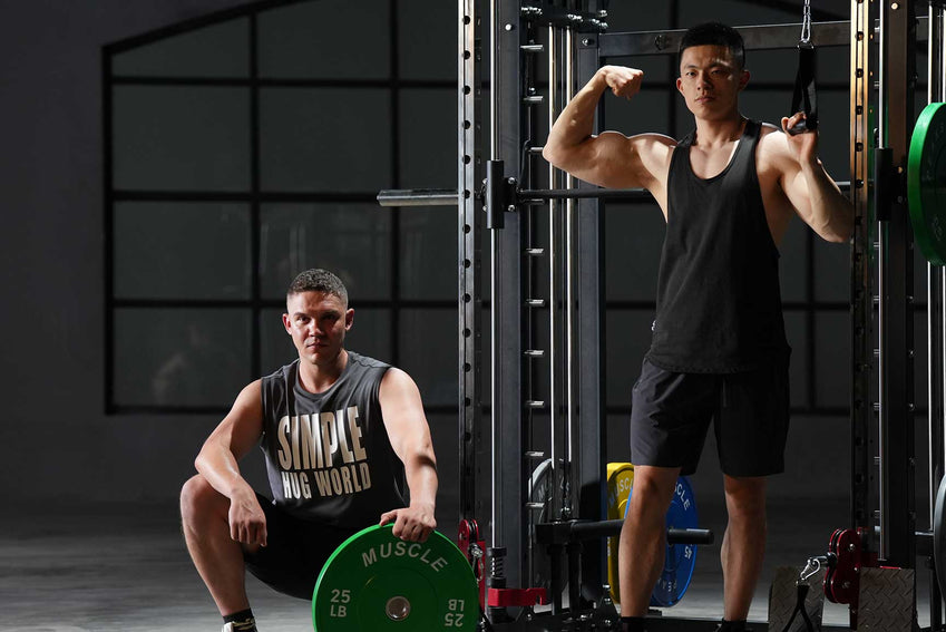 A man is showing his muscle before the smith machine. A man is siting near the smith machine
